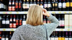 A woman at the supermarket can't decide which wine to choose - wine shopping needs video assistance